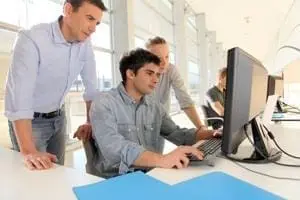 Three colleagues gather around a desktop computer, collaborating in a bright office space.