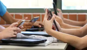 Close-up of several people’s hands holding smartphones over a desk with papers and a tablet nearby.