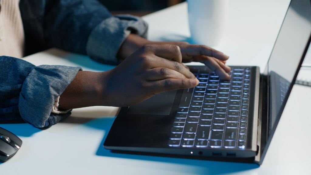 Person typing on a laptop at a bright desk, with a wireless mouse nearby.
