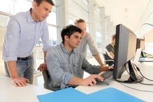 Three colleagues gather around a desktop computer, collaborating in a bright office space.